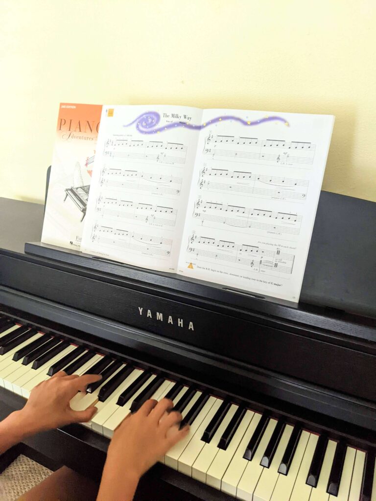 child's hands on piano keys with Faber Piano Adventures book open to song
