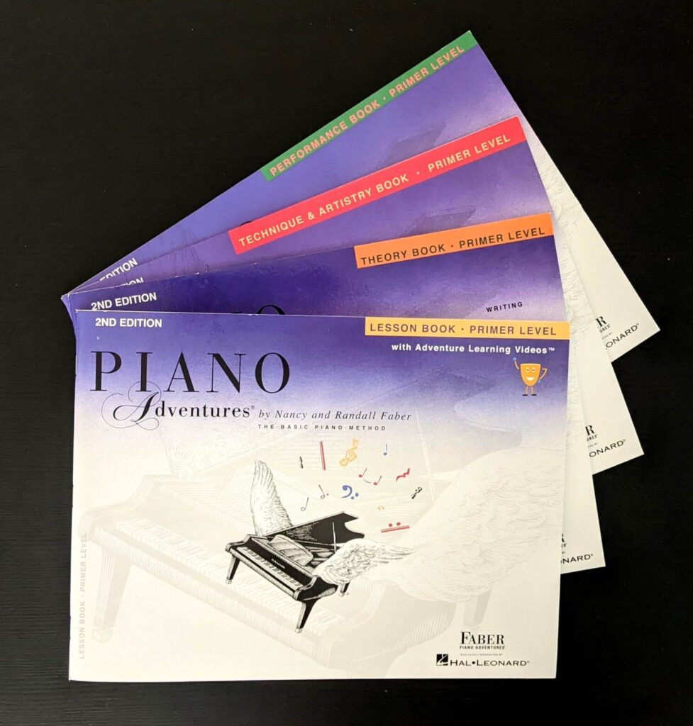 Four Piano Adventures Primer Level Books laid out on a black background